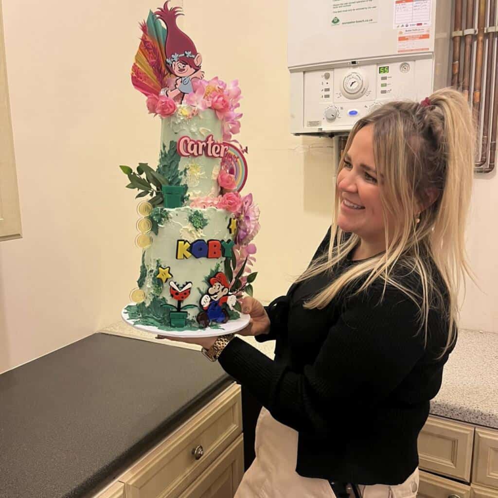 Colorful birthday cake with decorations being held my a women in a kitchen. 