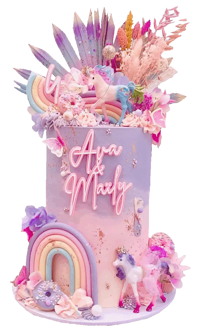 Tall unicorn-themed birthday cake featuring a custom pink acrylic name charm reading 'Ava & Marly', styled with decorative dried purple palm spears, pink bunny tail florals, and pastel rainbow cake toppers.